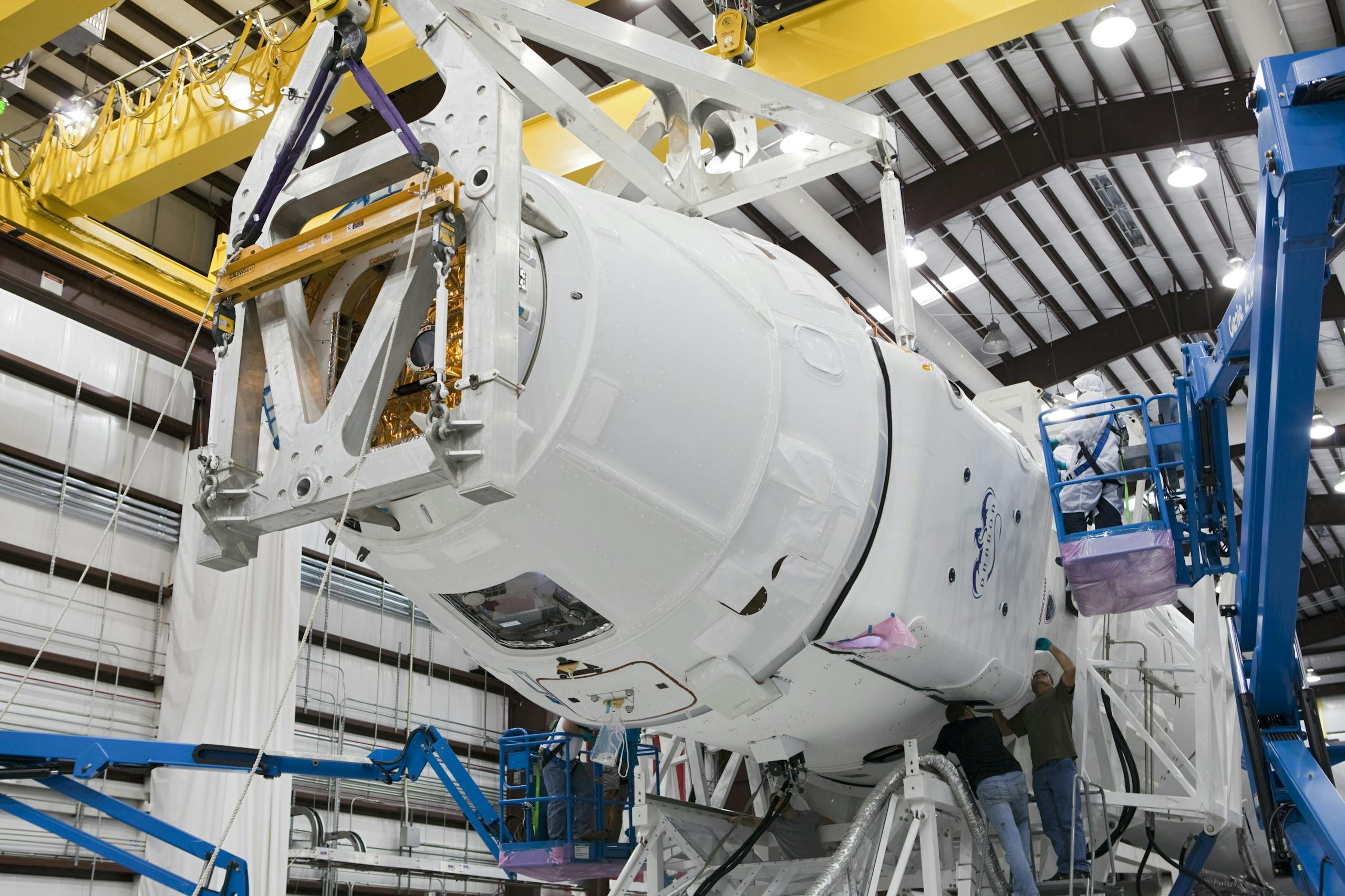 Technicians work on spacecraft assembly in an industrial facility with high-tech equipment.